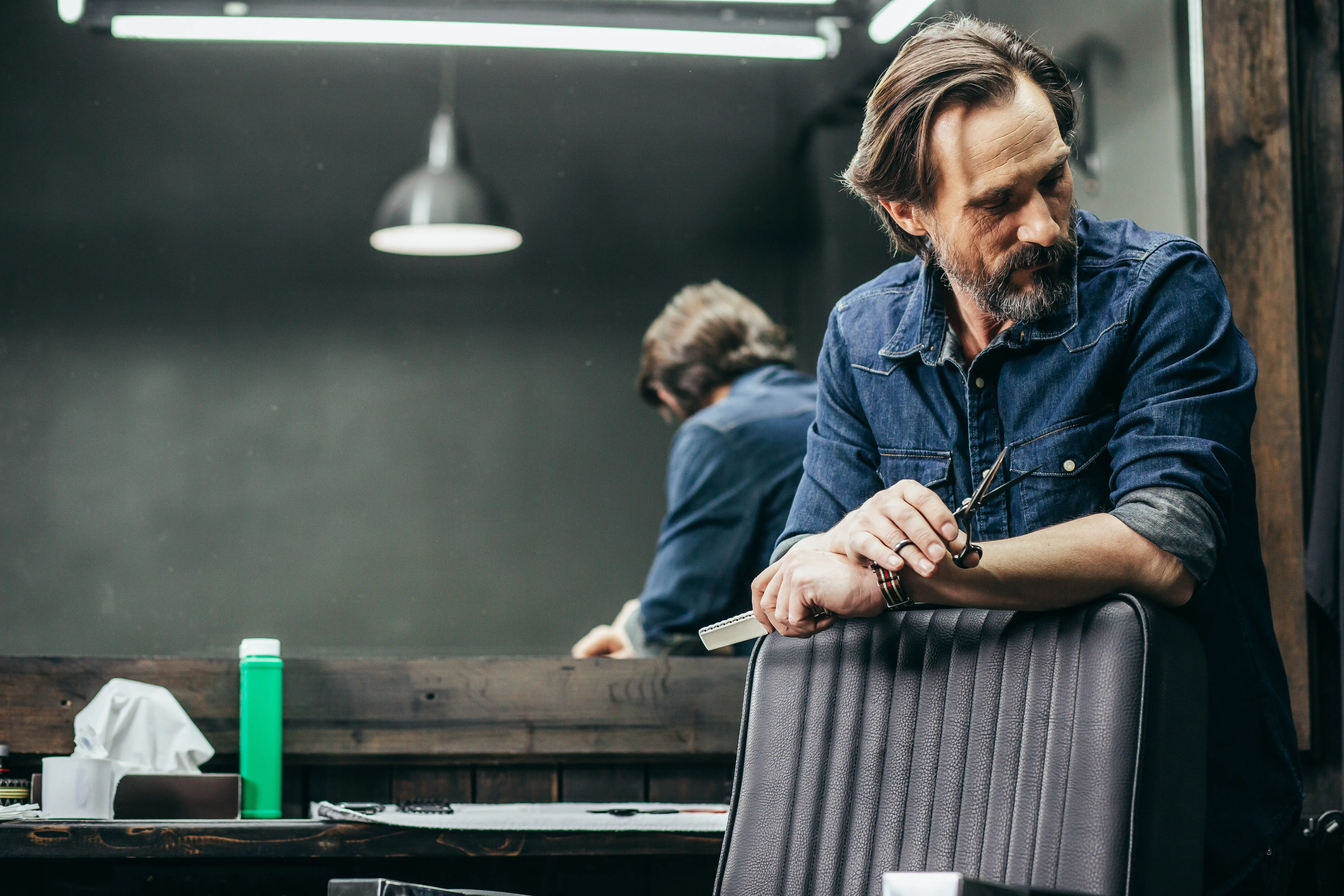 A barber stands next to the armchair, holding scissors.