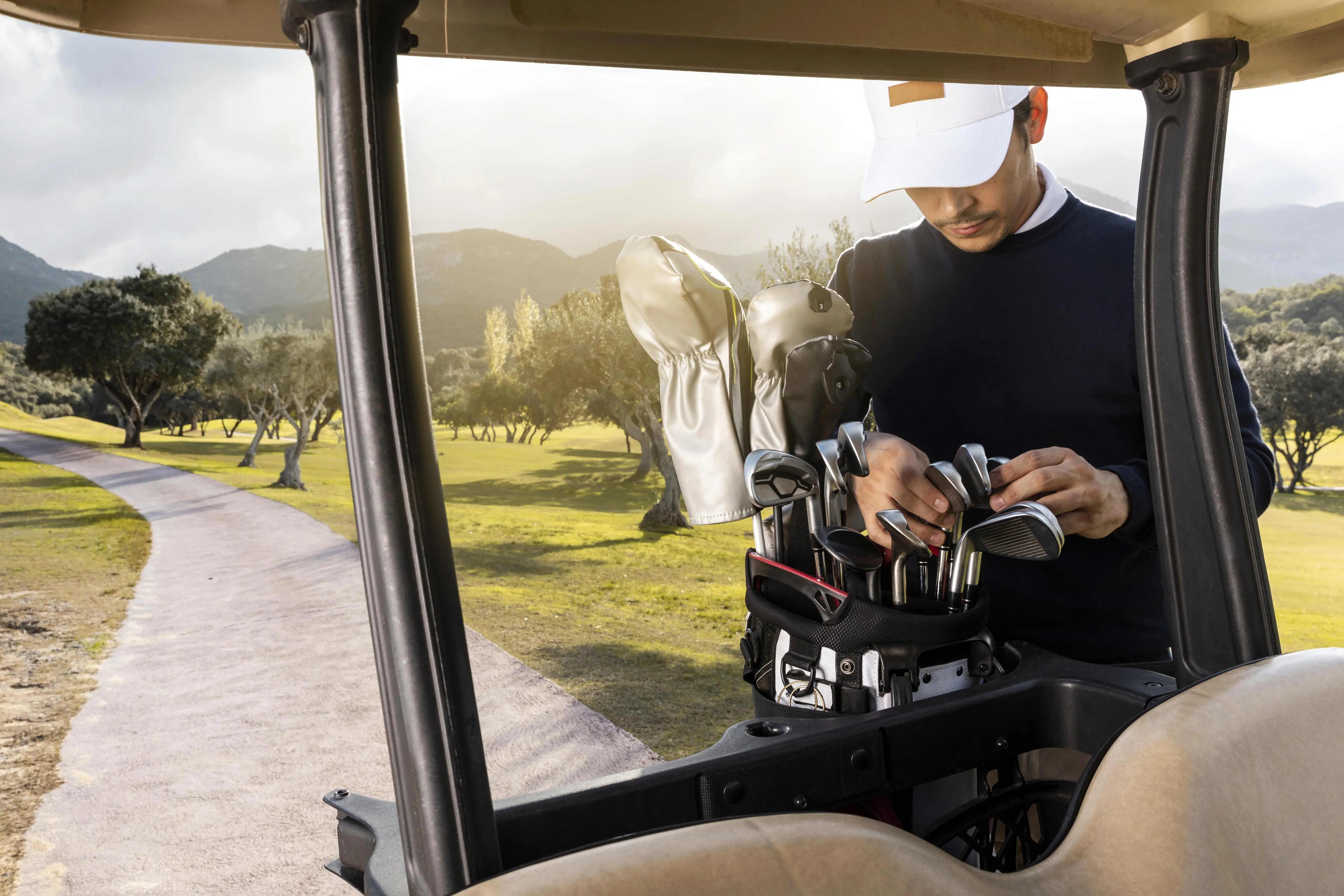 Frontal view of a man with golf clubs beside a golf cart.