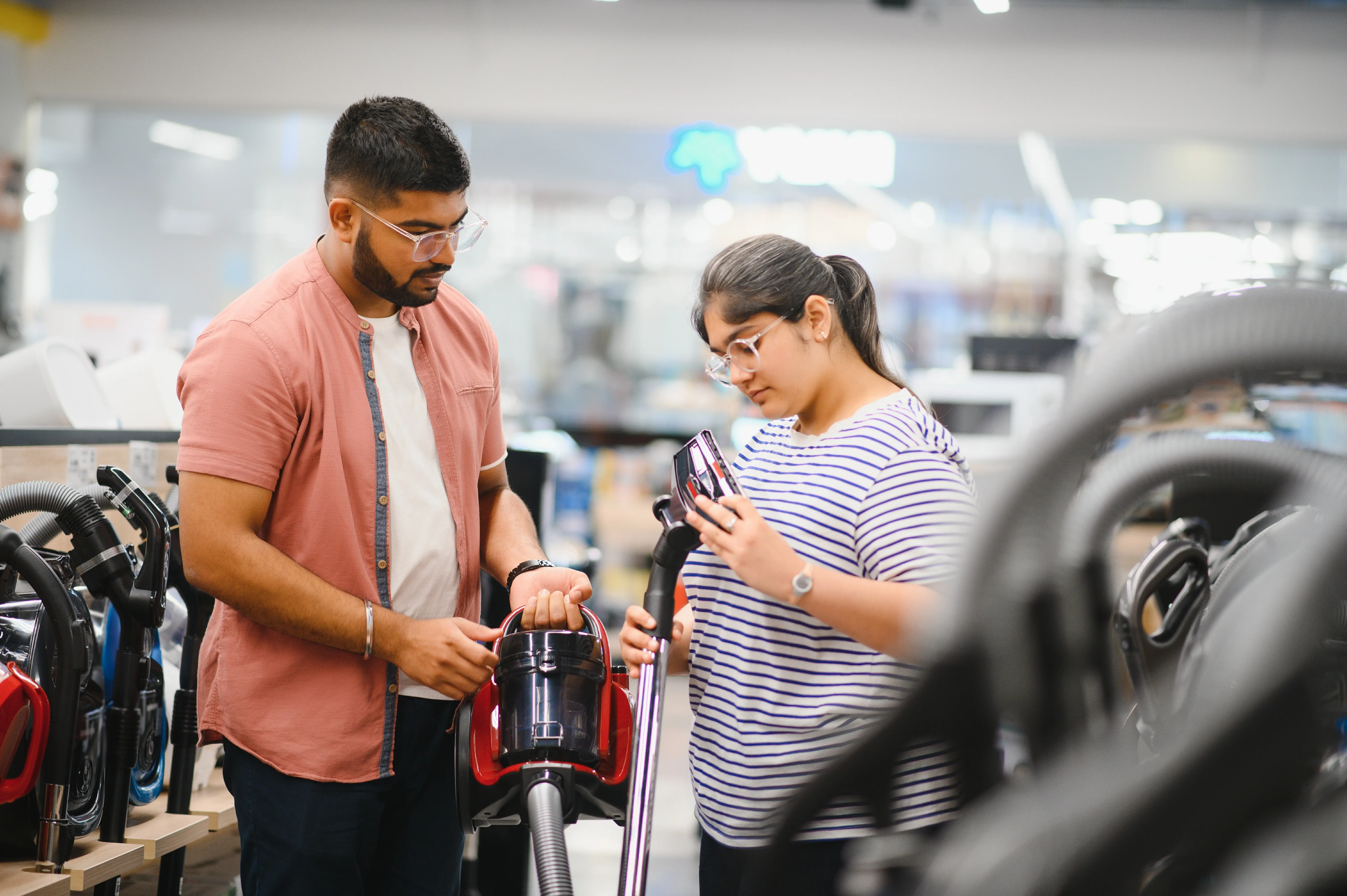 A young Indian couple purchases a vacuum cleaner at an electronics store.